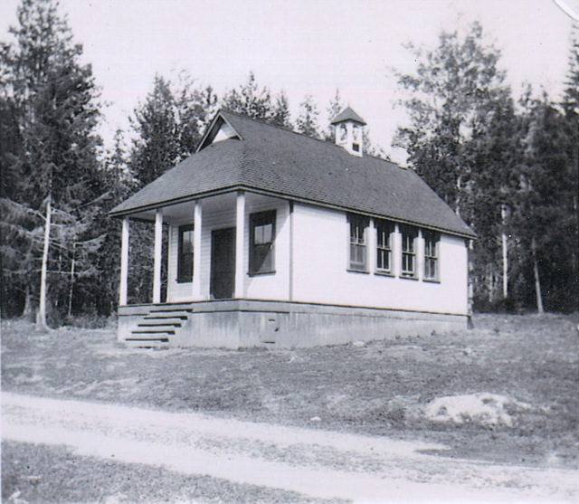 A historical black and white photo of the Park Siding School, showing its classic one-room schoolhouse design with a bell tower, surrounded by a natural forest landscape. The image captures a serene educational setting from a bygone era.