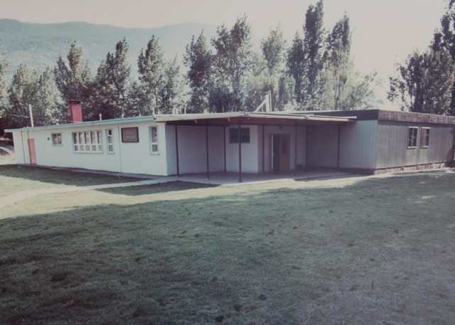 A vintage color photograph of Montrose Elementary, capturing the mid-20th-century architectural style of a single-story school building set against a backdrop of lush trees and distant hills, highlighting the rural educational environment of the time.