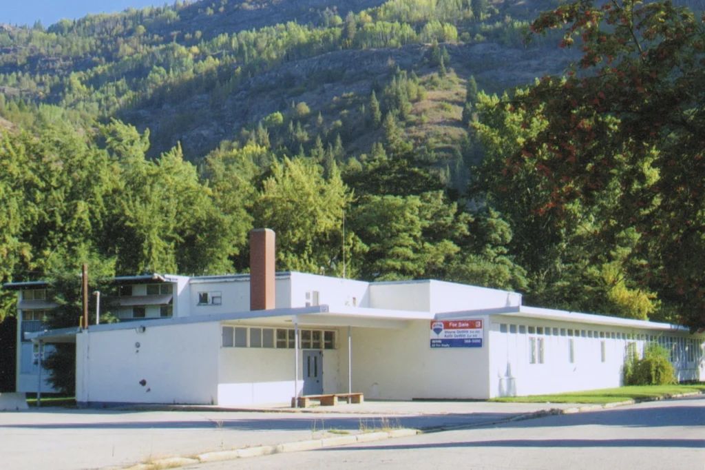 A color photograph of Sunningdale School, a single-story educational building with a flat roof, large windows, and a simple design, set against a backdrop of forested mountains, exemplifying mid-20th-century school architecture in a serene natural environment.