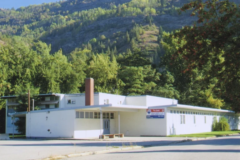 A color photograph of Sunningdale School, a single-story educational building with a flat roof, large windows, and a simple design, set against a backdrop of forested mountains, exemplifying mid-20th-century school architecture in a serene natural environment.