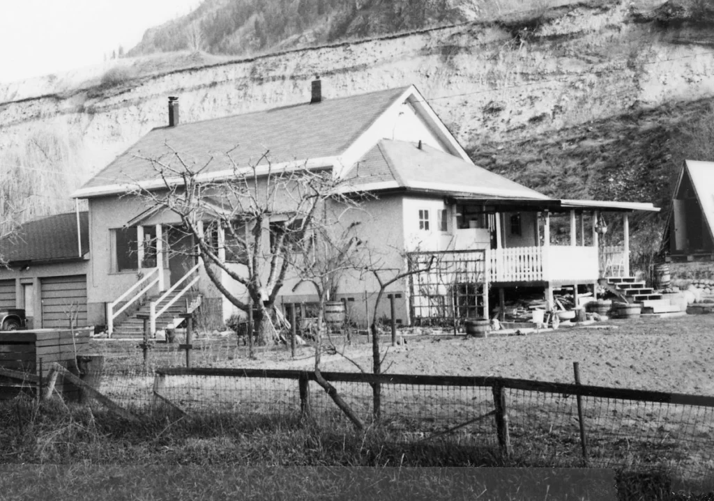 A black and white photo of Brilliant School No. 1, showing a gabled, two-story building with a covered front porch, typical of the rural school architecture from an earlier period, with a backdrop of a high earthen cliff that underscores the natural and somewhat isolated setting of the school.