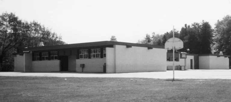 A black and white photograph from 1992 showing Castlegar Primary School, characterized by its single-story, flat-roofed structure, large windows, and an outdoor play area complete with a basketball hoop, portraying a typical educational setting of the late 20th century.